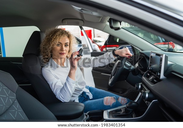 Confident\
woman with key sitting in new car at\
dealership