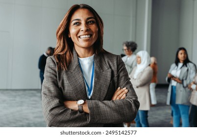 Confident woman leader standing proudly at a business conference in an office environment. Diverse group of professionals discussing in the background. - Powered by Shutterstock