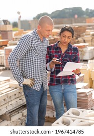 Confident Woman Manager Discussing Order List With Man Worker At Warehouse Of Building Materials