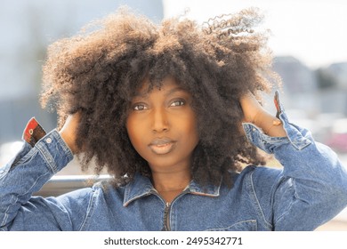 A confident woman with natural afro hair poses stylishly outdoors in a denim jacket, exuding boldness and beauty - Powered by Shutterstock