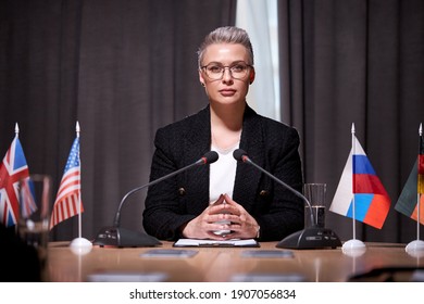 Confident Woman Sits With Microphone Holding Business Meeting, In Formal Wear, Sits At Desk In Boardroom Discussing Business Ideas And Strategies