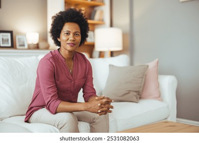 A confident woman sits on a cozy sofa in a warmly lit living room, exuding relaxation and tranquility. The modern decor complements the peaceful atmosphere. - Powered by Shutterstock