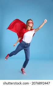 Confident Woman Wearing Superhero Cape And Mask On Light Blue Background