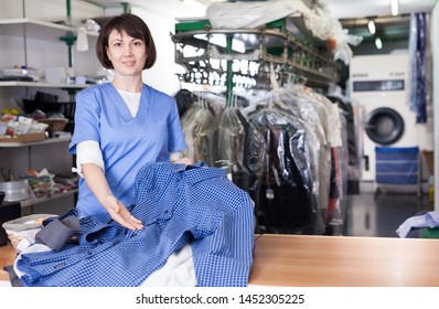 Confident Woman Worker Of Dry Cleaner Standing At Reception Counter, Showing Clean Shirts After Dry Cleaning