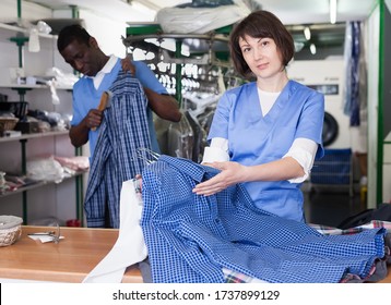 Confident Woman Worker Of Dry Cleaner Standing At Reception Counter, Showing Clean Shirts After Dry Cleaning