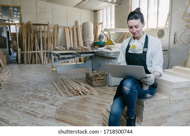 Confident Woman Working As Carpenter In Her Own Woodshop. She Using A Laptop And Writes Notes While Being In Her Workspace. Small Business Concept.