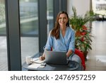 Confident woman working remotely on a laptop in a modern office with greenery and technology