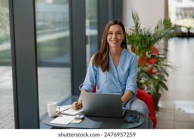 Confident woman working remotely on a laptop in a modern office with greenery and technology