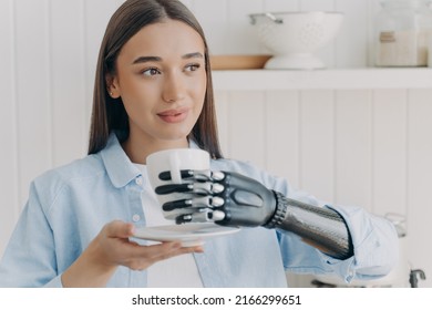 Confident women with disability is holding cup of tea with cyber hand. Happy girl with disability at kitchen at home. Pretty woman with makeup is smiling. Concept of grasp sensors in modern electronic