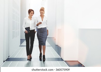 Confident Women Reading Information About Finance News While Walking In Company Hallway During Work Break, Successful Businesswoman Writing Text Message Her Client While Goes With Secretary To Office 