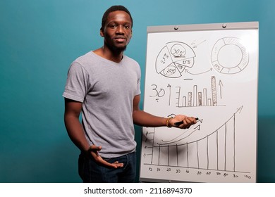 Confident worker using whiteboard to make business presentation, standing in front of camera. Young person promoting financial statistics on placard for economy growth in studio.