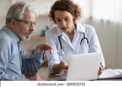 Confident young 30s female general practitioner physician showing medical insurance program presentation or health lab test results on computer to focused middle aged older patient at clinic meeting.