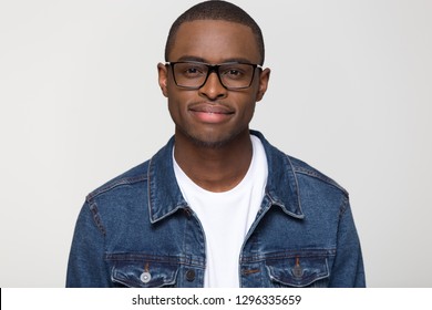 Confident young african american man wearing denim jacket and glasses looking at camera smiling, black handsome millennial smart male guy nerd isolated on blank grey white studio background, portrait
