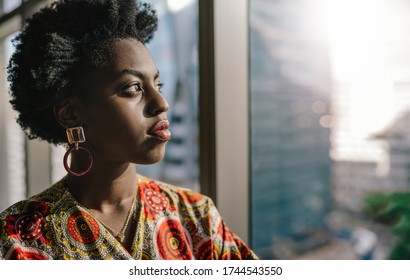 Confident young African businesswoman looking out at the city skyline through an office building window - Powered by Shutterstock