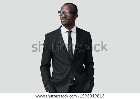 Confident young African man in formalwear looking away while standing against grey background