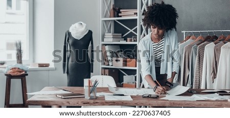 Confident young African woman working on sketches in fashion design studio