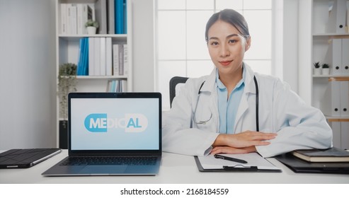 Confident Young Asia Female Doctor In White Medical Uniform With Stethoscope Looking At Camera And Showing Laptop Computer In Health Hospital. Consulting And Therapy Concept.