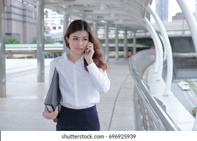 Confident young Asian business woman talking on phone while walking on walkway of modern city.