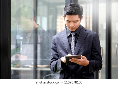 Confident young Asian businessman working on digital tablet while standing in office  - Shutterstock ID 1159378105