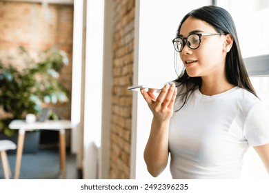 Confident young asian girl student smm manager social media worker freelancer intern businesswoman recording voice message on her phone talking with customers partners colleague at the workplace - Powered by Shutterstock