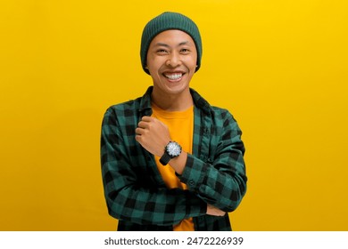 Confident young Asian man, clad in a beanie hat and casual outfit, stands with folded arms, wearing a confident smile as he gazes at the camera while standing against a yellow background - Powered by Shutterstock