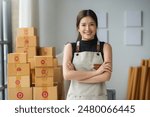 Confident young asian woman in her 20s, business owner, stands in storage room filled with packages, smiling proudly at successful startup venture