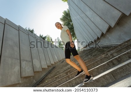 Confident young Asian woman in stylish tracksuit stands on stone staircase after training at sunrise on street low angle shot