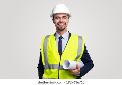 Confident young bearded male construction engineer in hardhat and waistcoat over formal suit holding rolled blueprint and looking at camera with smile against white background