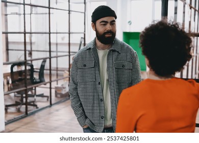 Confident young bearded male and curly haired female colleagues standing in modern office while discussing business strategy on project in modern office and looking at each other - Powered by Shutterstock