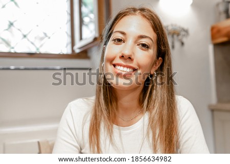 Confident young beautiful woman smiling looking at the camera for a video call conference in her home - Portrait of a cute long hair female alone person at home - New normal social communication