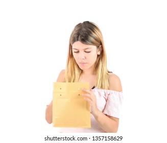Confident Young Blonde Teenager Girl Opening A Brown Envelope Against A White Background
