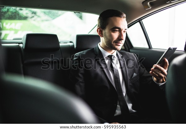 Confident young businessman\
setting his smart phone and looking at camera while sitting in the\
car