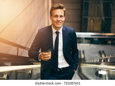 Confident young businessman smiling while drinking a coffee and riding up an escalator in a subway station during his morning commute - Powered by Shutterstock