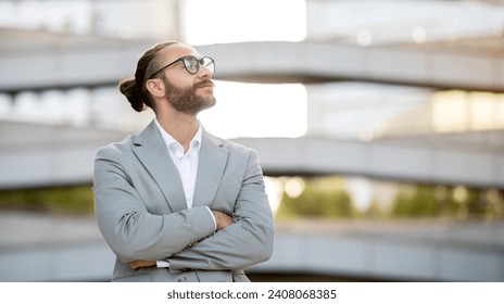 Confident young businessman in suit standing outdoors and looking upwards, handsome male entrepreneur with crossed arms embodying vision and ambition, posing against modern architectural backdrop - Powered by Shutterstock