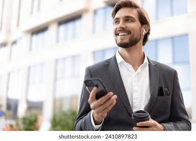 Confident young businessman using cell phone and drinking coffee in the city - Powered by Shutterstock