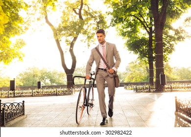 Confident young businessman walking with bicycle on the street in town 