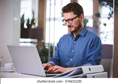 Confident young businessman working on laptop at creative office - Shutterstock ID 574631230
