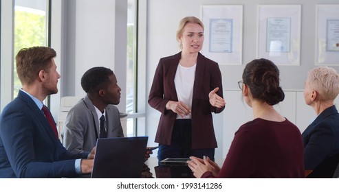 Confident Young Businesswoman Giving Presentation To Team In Office. Female Executive Leading Corporate Business Meeting With Multiethnic Colleagues In Modern Office