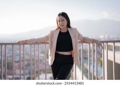 Confident young businesswoman leans against a railing on a rooftop, overlooking a sprawling cityscape, enjoying the urban vista and contemplating future opportunities - Powered by Shutterstock