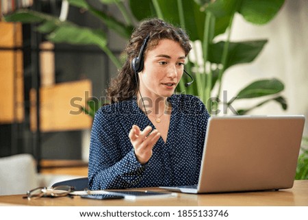 Confident young businesswoman wearing headphones and discussing project details with clients on video call. Skilled woman worker with headphones conducting online meeting with colleagues.