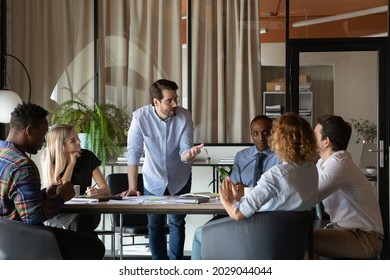 Confident young Caucasian businessman hold lead meeting with diverse multiethnic employees colleagues in office. Motivated male leader or boss talk at team negotiation briefing. Leadership concept. - Shutterstock ID 2029044044