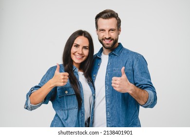 Confident young caucasian couple man and woman husband and wife spouses boyfriend and girlfriend showing thumbs up looking at camera isolated in white background. Quality check