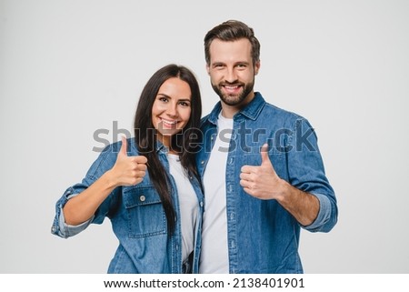 Confident young caucasian couple man and woman husband and wife spouses boyfriend and girlfriend showing thumbs up looking at camera isolated in white background. Quality check