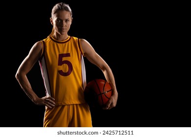 Confident young Caucasian female basketball player poses in basketball attire, with copy space on black background. Her athletic stance and focused gaze emphasize determination and skill in sports. - Powered by Shutterstock