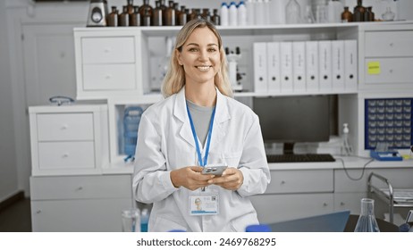 Confident young caucasian woman scientist with blonde hair in a white lab coat using a smartphone in a laboratory. - Powered by Shutterstock