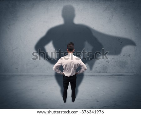 A confident young elegant salesman with briefcase facing a wall, looking at his superman shadow concept