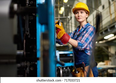 Confident Young Engineer Wearing Overall And Checked Shirt Looking Away While Carrying Out Inspection At Manufacturing Plant, Blurred Background