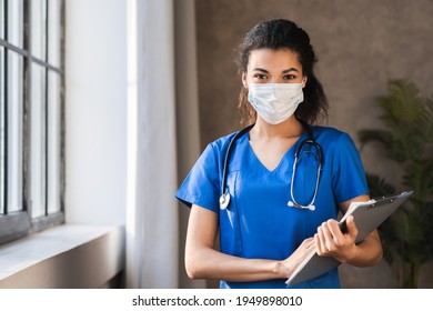 Confident Young Female African Scrub Nurse Wear Blue Uniform, Face Mask,standing Arms Crossed In Hospital Hallway. Black Millennial Woman Doctor, Surgeon, Medic Staff Professional Portrait.