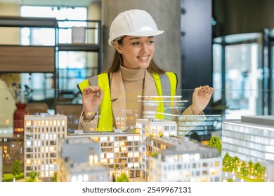 Confident young female architect in hardhat and reflective vest analyzing looking at business office complex architectural model. Woman in protective clothing designer of buildings working in office. - Powered by Shutterstock