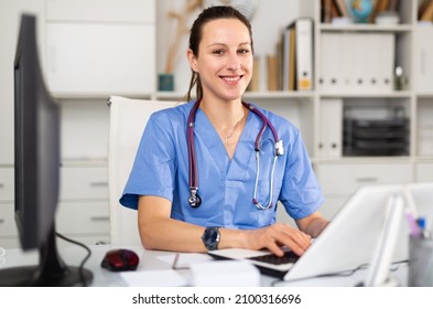 Confident Young Female Doctor Prints An Outpatient Patient Card On A Computer In The Office, Sitting At Her Workplace